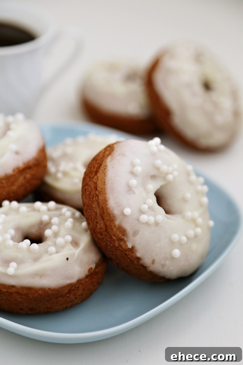 Pillowy Pumpkin Doughnuts with Dreamy Cream Cheese Frosting 5 Decorated pumpkin donuts with cream cheese glaze and edible pearls, on a serving plate.