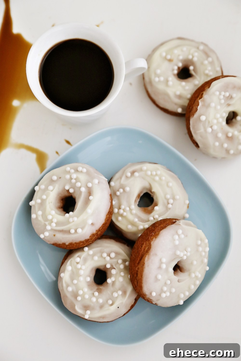Pillowy Pumpkin Doughnuts with Dreamy Cream Cheese Frosting 6 Two pumpkin donuts with glaze, one casually placed next to a coffee spill, creating an artsy scene.
