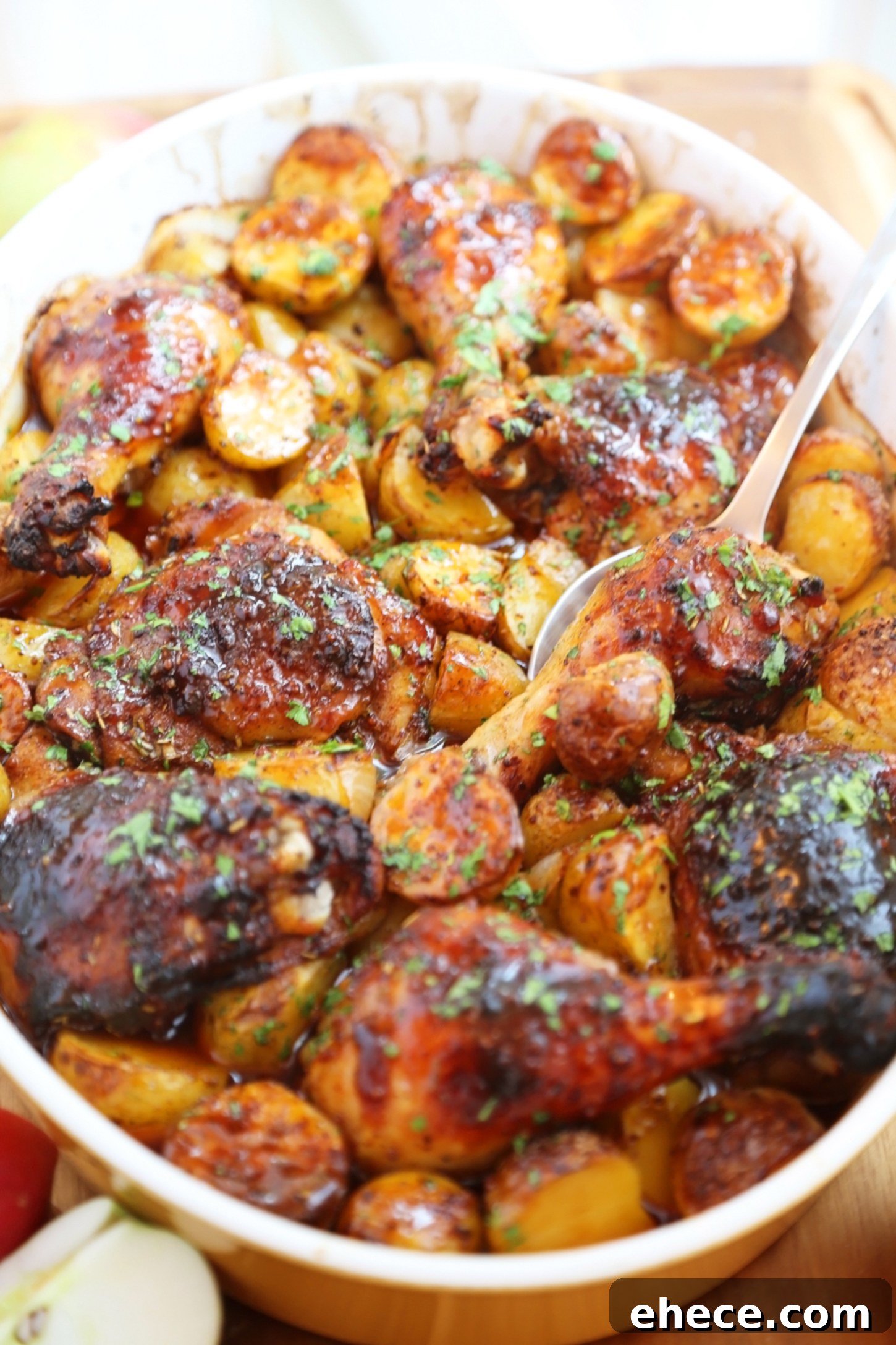 Close-up of golden-brown roasted apple cider chicken with potatoes and onions in a baking dish, garnished with fresh herbs.