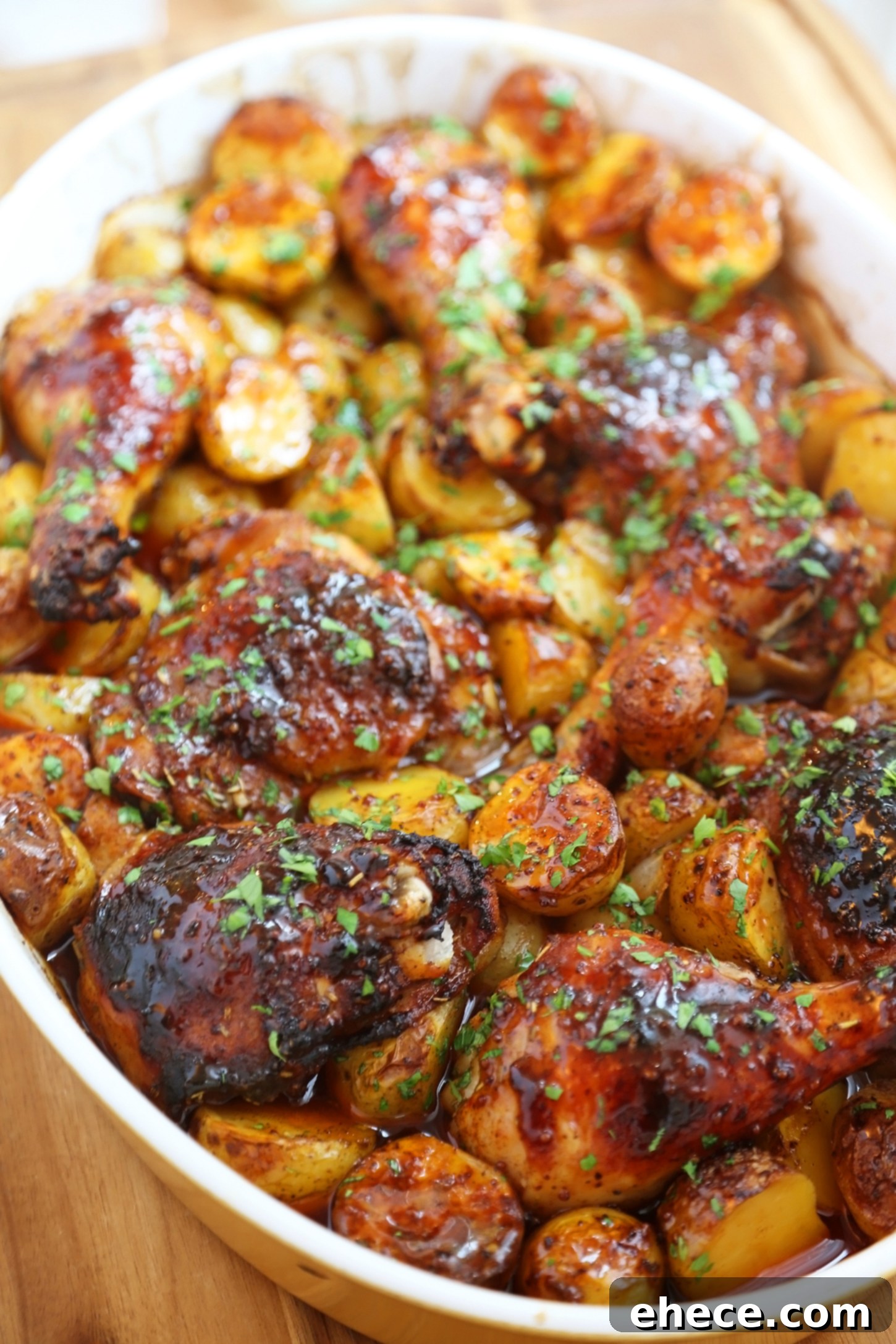 Overhead view of roasted apple cider chicken legs and thighs with baby potatoes and sliced onions, glistening with glaze.