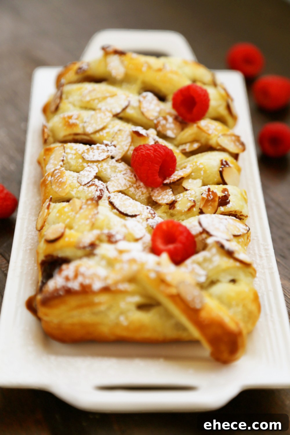 A slice of the warm chocolate puff pastry braid being lifted, showing the molten dark chocolate oozing out, garnished with fresh raspberries.