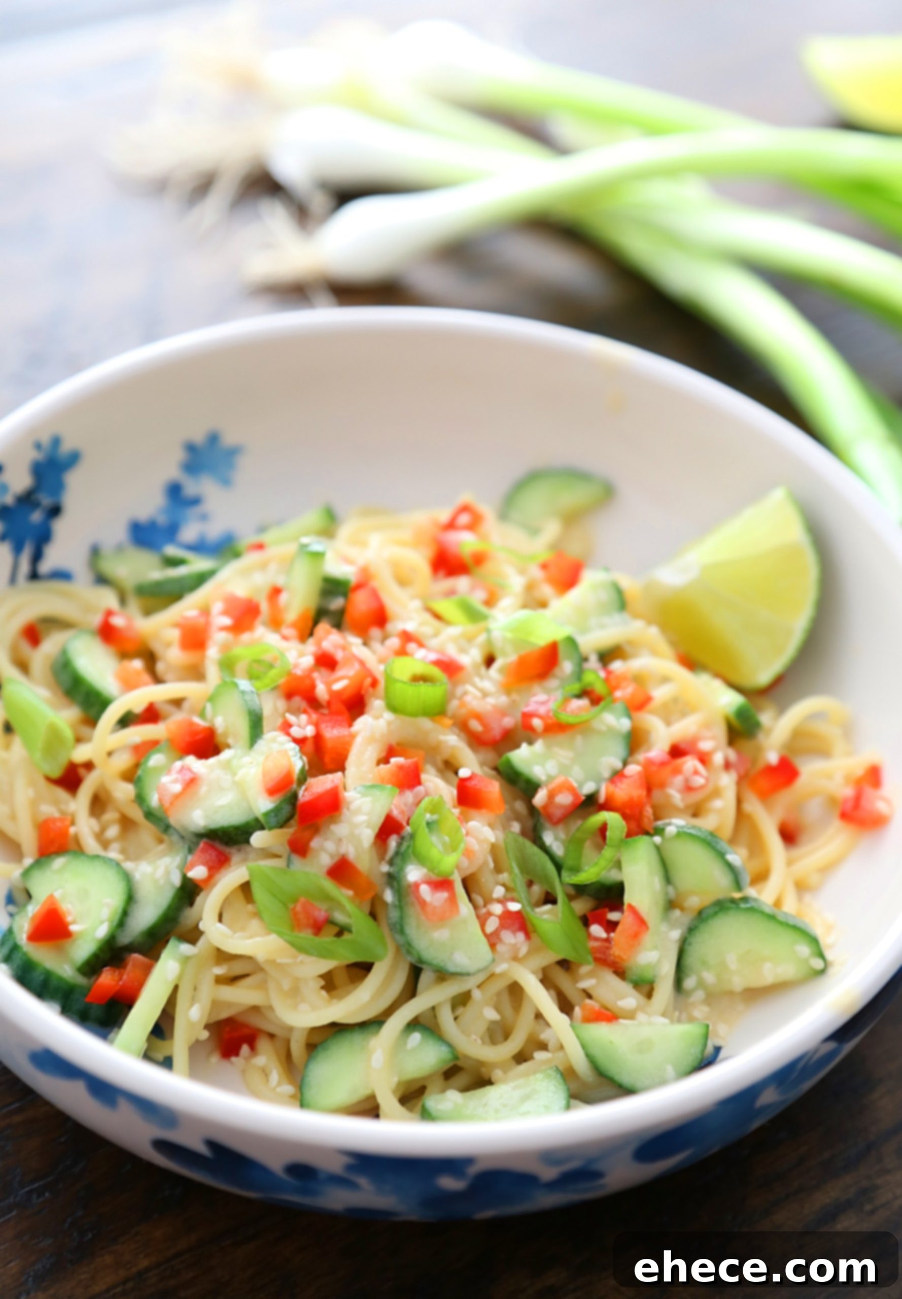 Overhead shot of two bowls of Cold Sesame Cucumber Noodle Salad on a rustic wooden table.