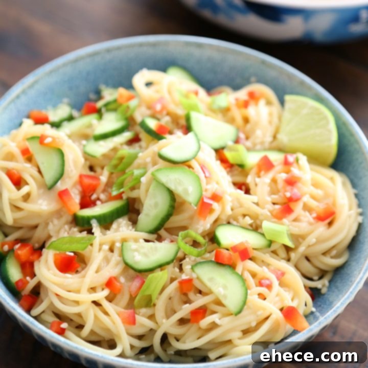 A bowl of Cold Sesame Cucumber Noodle Salad garnished with fresh herbs and lime wedges.