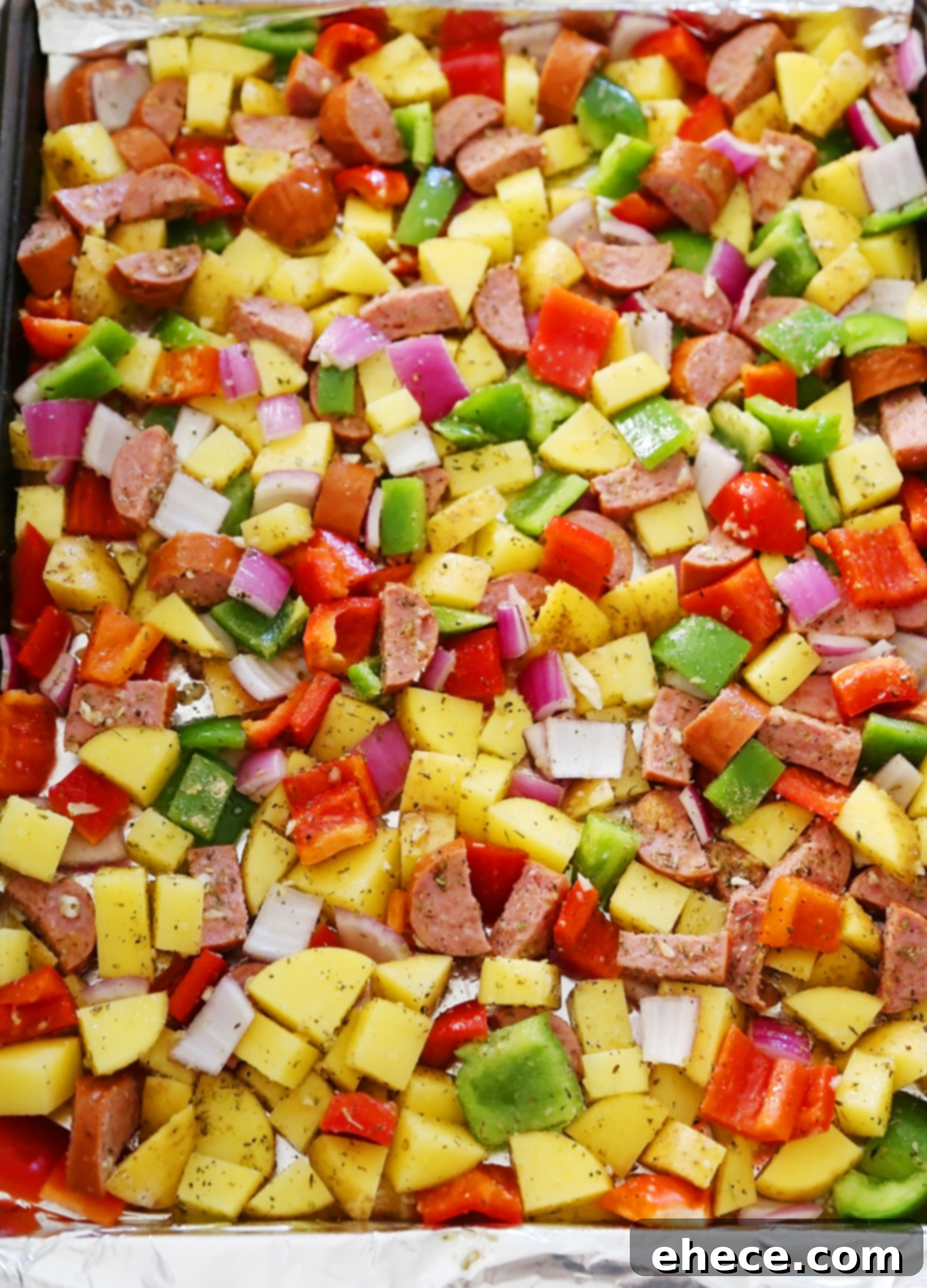 Close-up of freshly roasted sausage and mixed vegetables with potatoes on a baking sheet.