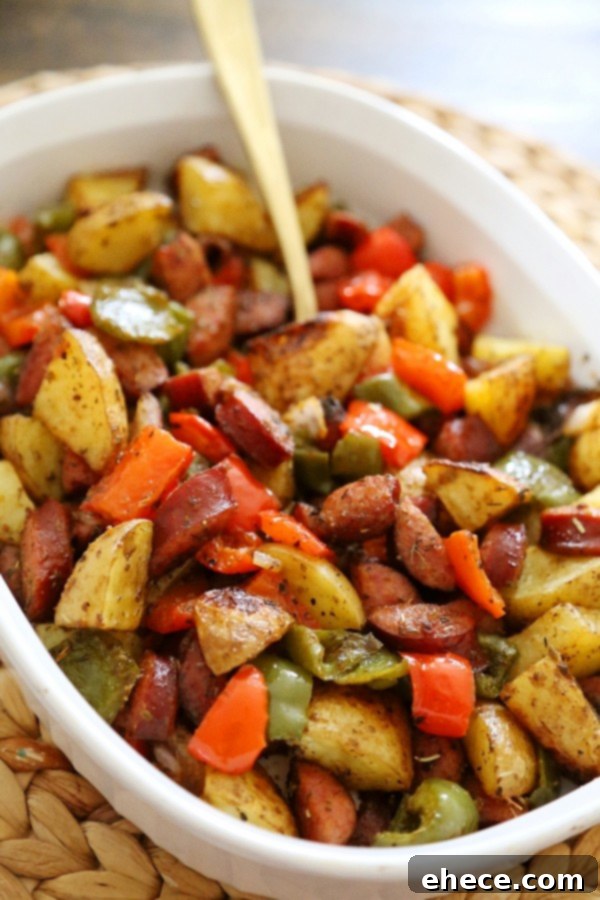 Close-up of a serving of roasted sausage, peppers, and potatoes in a white bowl, ready to eat.
