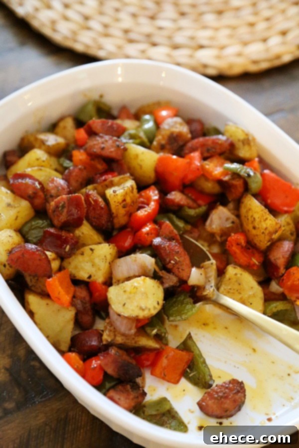 Appetizing shot of one-pan roasted sausage, peppers, and potatoes spread on a baking sheet.