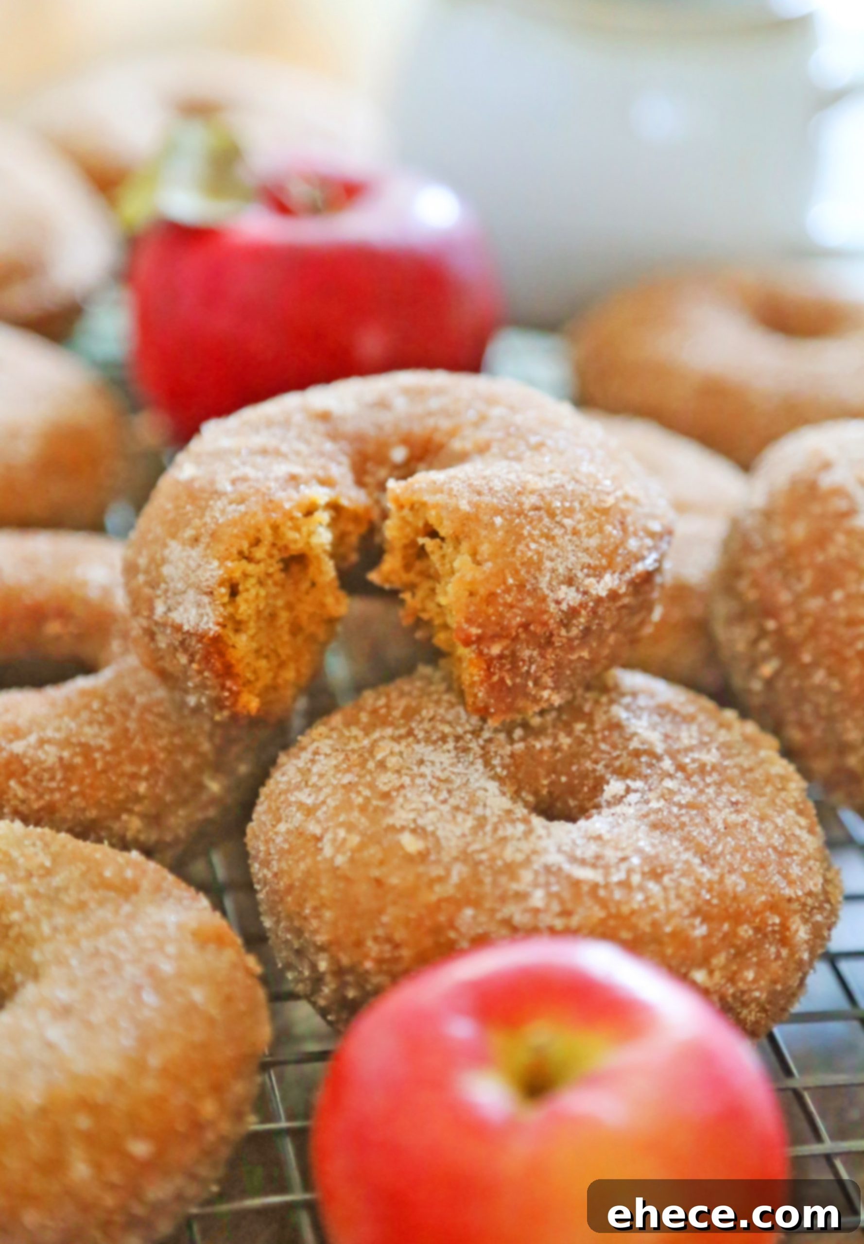 Close-up of a hand reaching for a baked apple cider donut, emphasizing its soft texture and delicious coating.