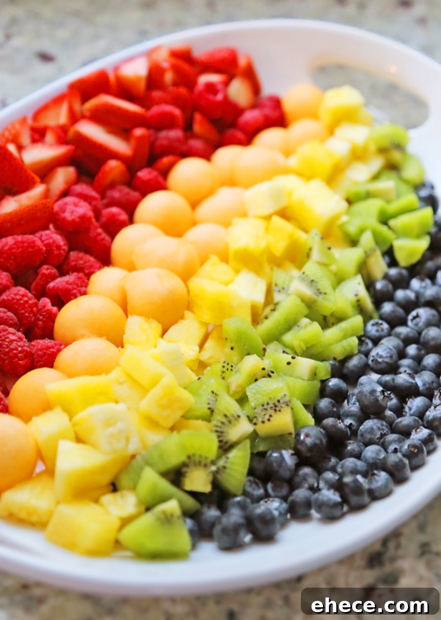 A vibrant platter of rainbow fruit salad featuring strawberries, raspberries, cantaloupe, pineapple, kiwi, and blueberries, perfect for a healthy meal or snack.