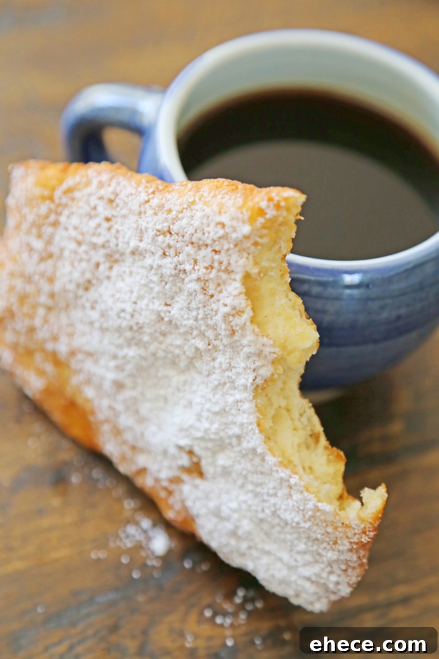 Three golden fried dough pieces on a wooden board, garnished with powdered sugar