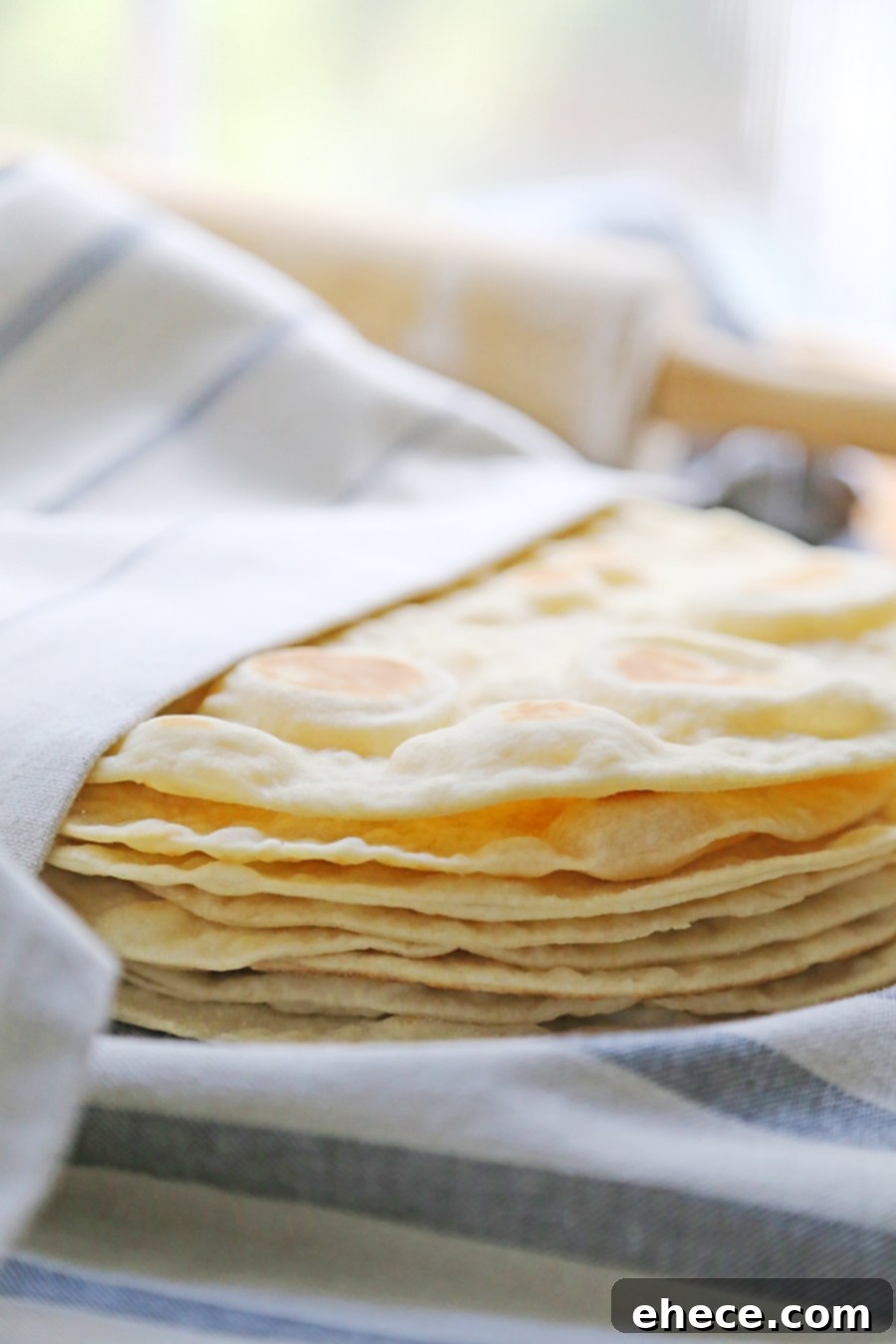 Pillowy Soft Homemade Flour Tortillas 6 A close-up shot of a stack of soft, warm homemade flour tortillas, enticing and ready to eat, with a few fresh ingredients in the background.