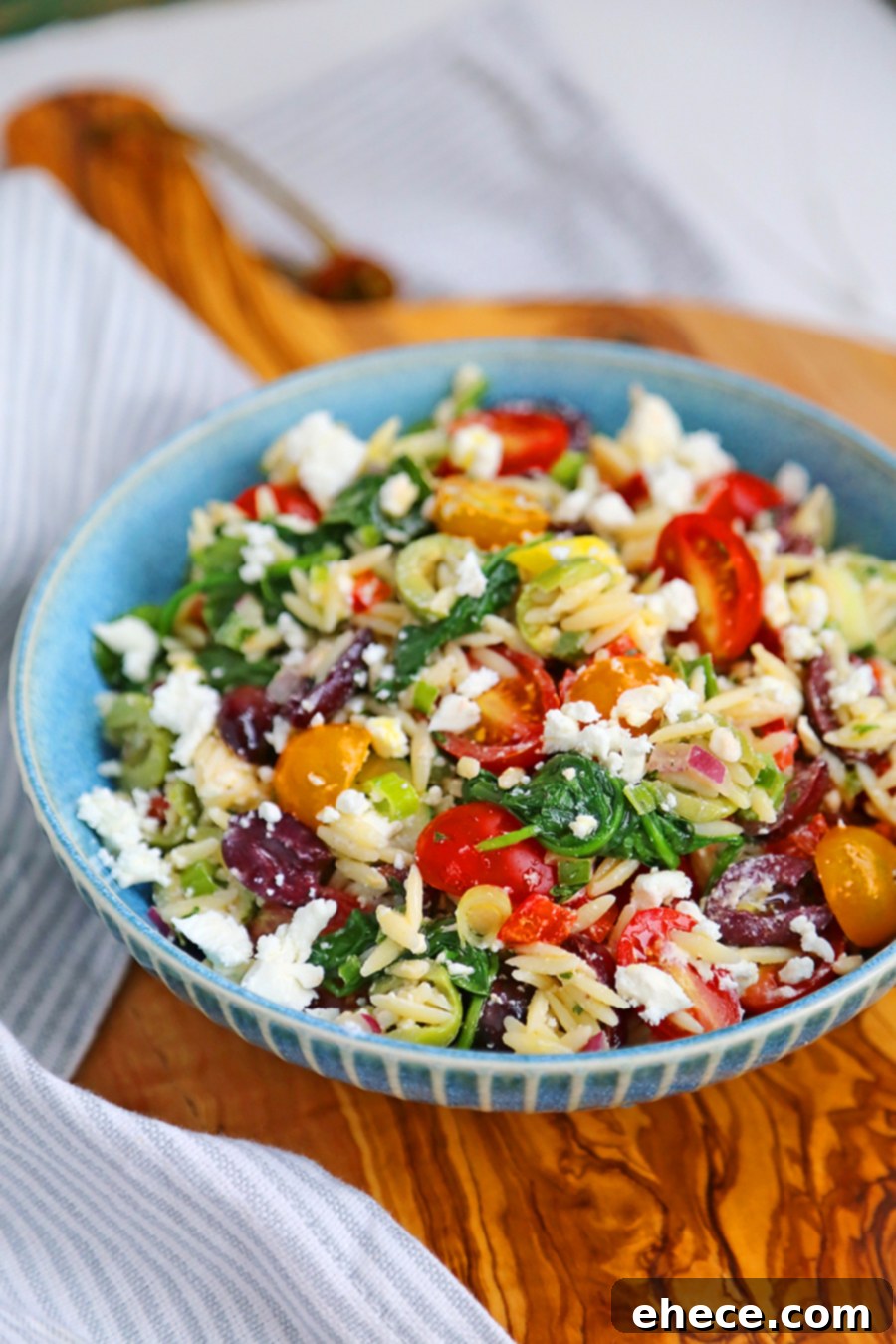 Mediterranean Sunshine Orzo Salad 4 A bowl of Mediterranean Orzo Salad on a wooden table, garnished with fresh herbs