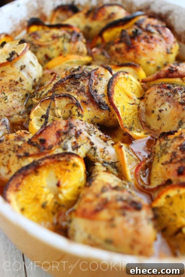 Whole roasted chicken surrounded by vibrant orange and lemon slices, with fresh rosemary and thyme sprigs.