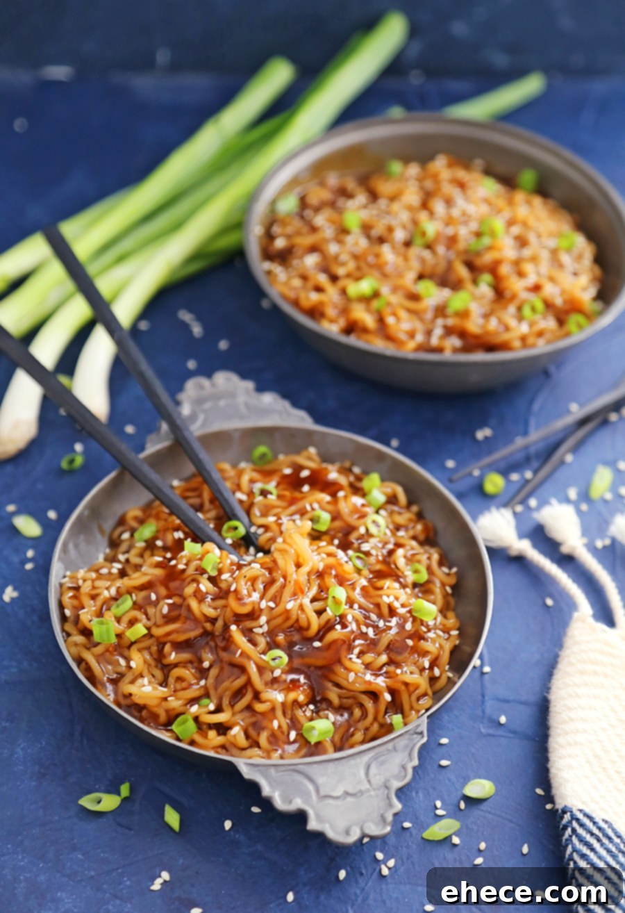 A vibrant bowl of saucy ramen noodles, garnished with sesame seeds and chopped scallions.