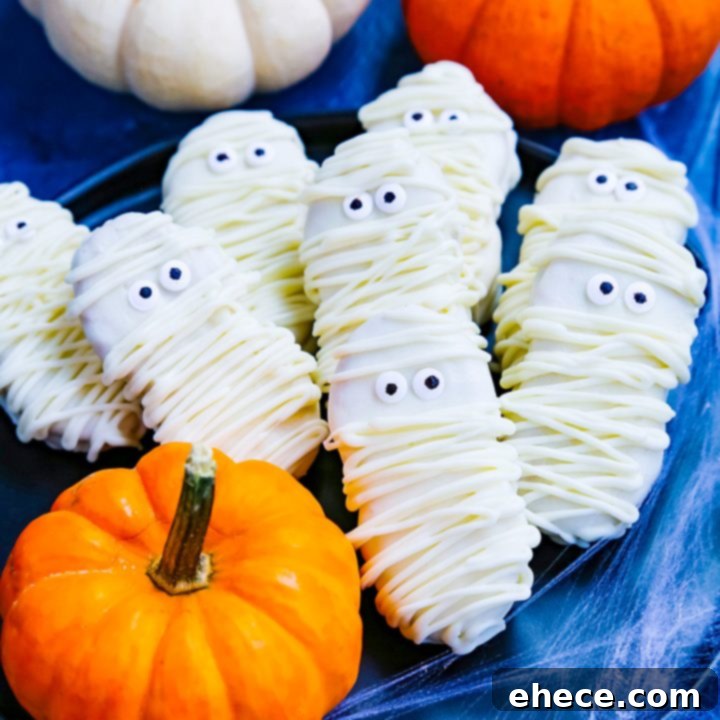 Close-up of a finished Nutter Butter Mummy Cookie with white chocolate bandages and candy eyes, on a white background.