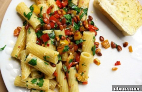 A plate of Rigatoni Peperonata garnished with fresh herbs and Parmesan cheese.