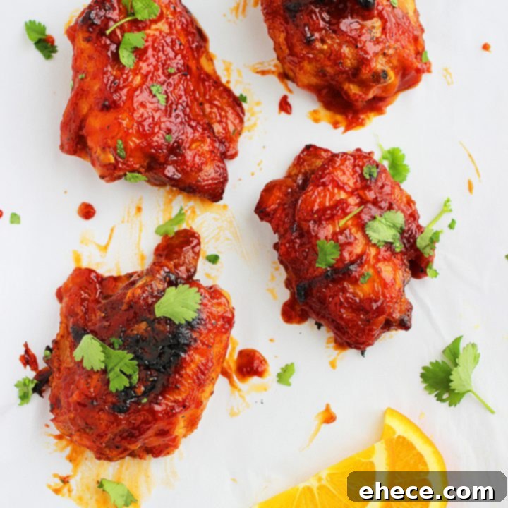 Zesty Orange Lacquered Chicken Thighs 2 Sticky Orange Glazed Chicken Thighs, garnished with fresh cilantro, ready to be served.