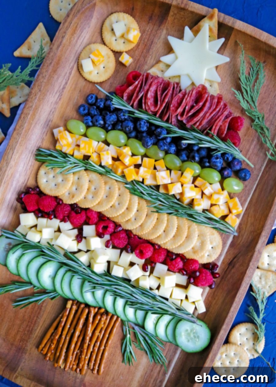 A close-up view of the Christmas Tree Charcuterie Board, highlighting the intricate arrangement of various cheeses, folded salami, fresh berries, and green grapes, all accented by fragrant rosemary sprigs and pretzel sticks at the base.
