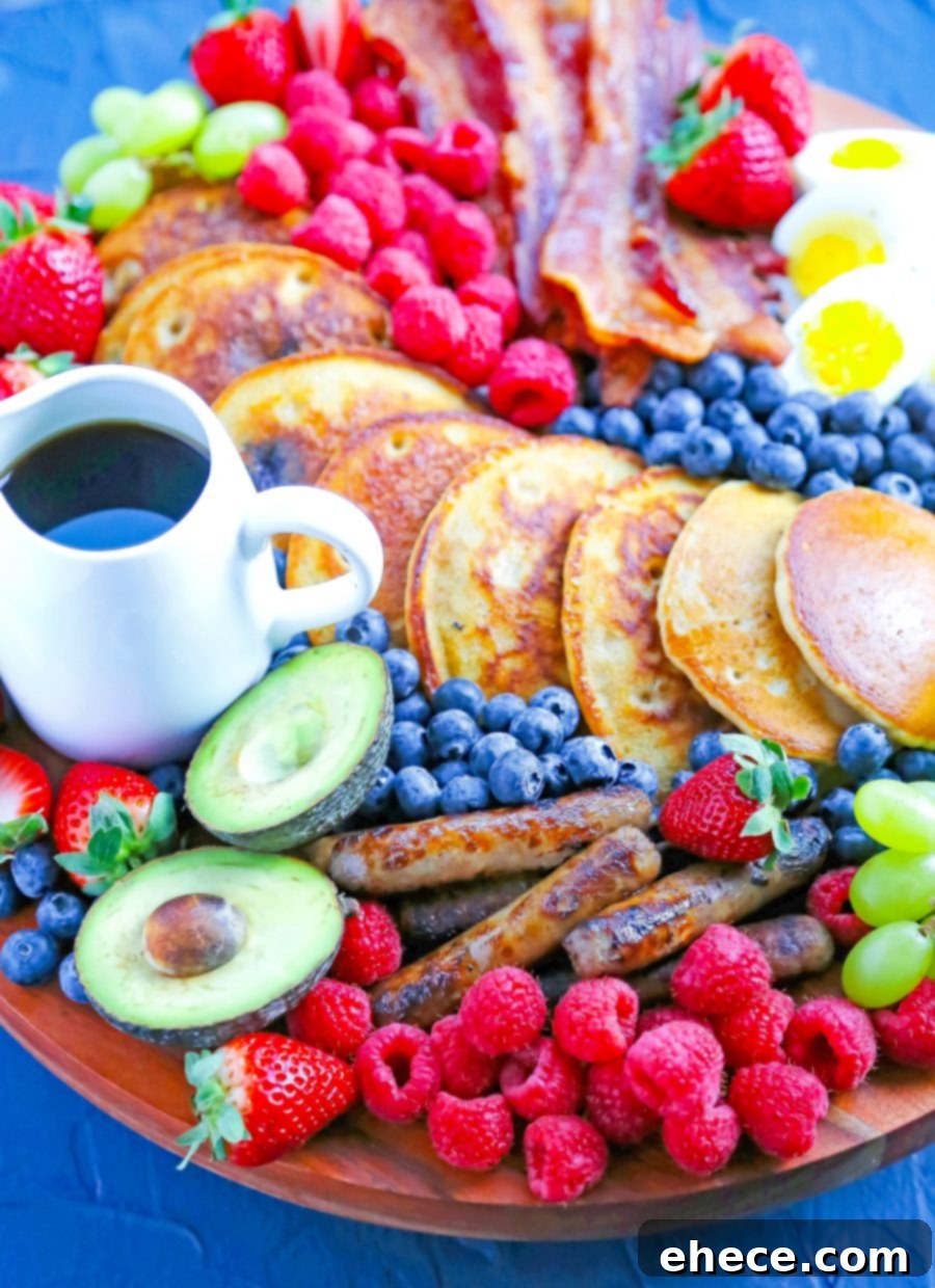 A close-up of a breakfast board showcasing an array of fruits like avocado slices, grapes, strawberries, and blueberries, alongside perfectly cooked pancakes and eggs.