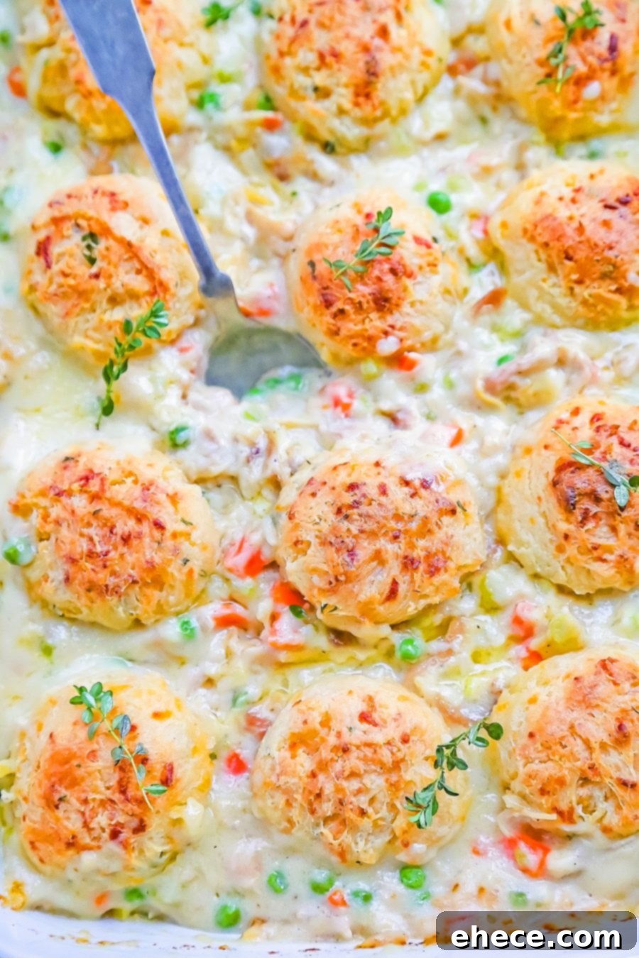 A close-up of a spoon scooping creamy Chicken Pot Pie with Cheddar-Chive Biscuits, highlighting the rich texture.