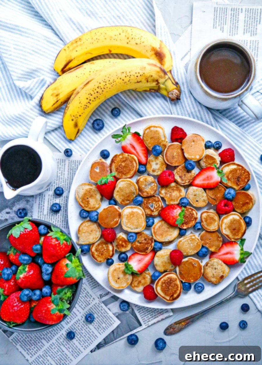 Deliciously golden-brown mini banana pancake bites stacked on a plate with fresh berries and maple syrup