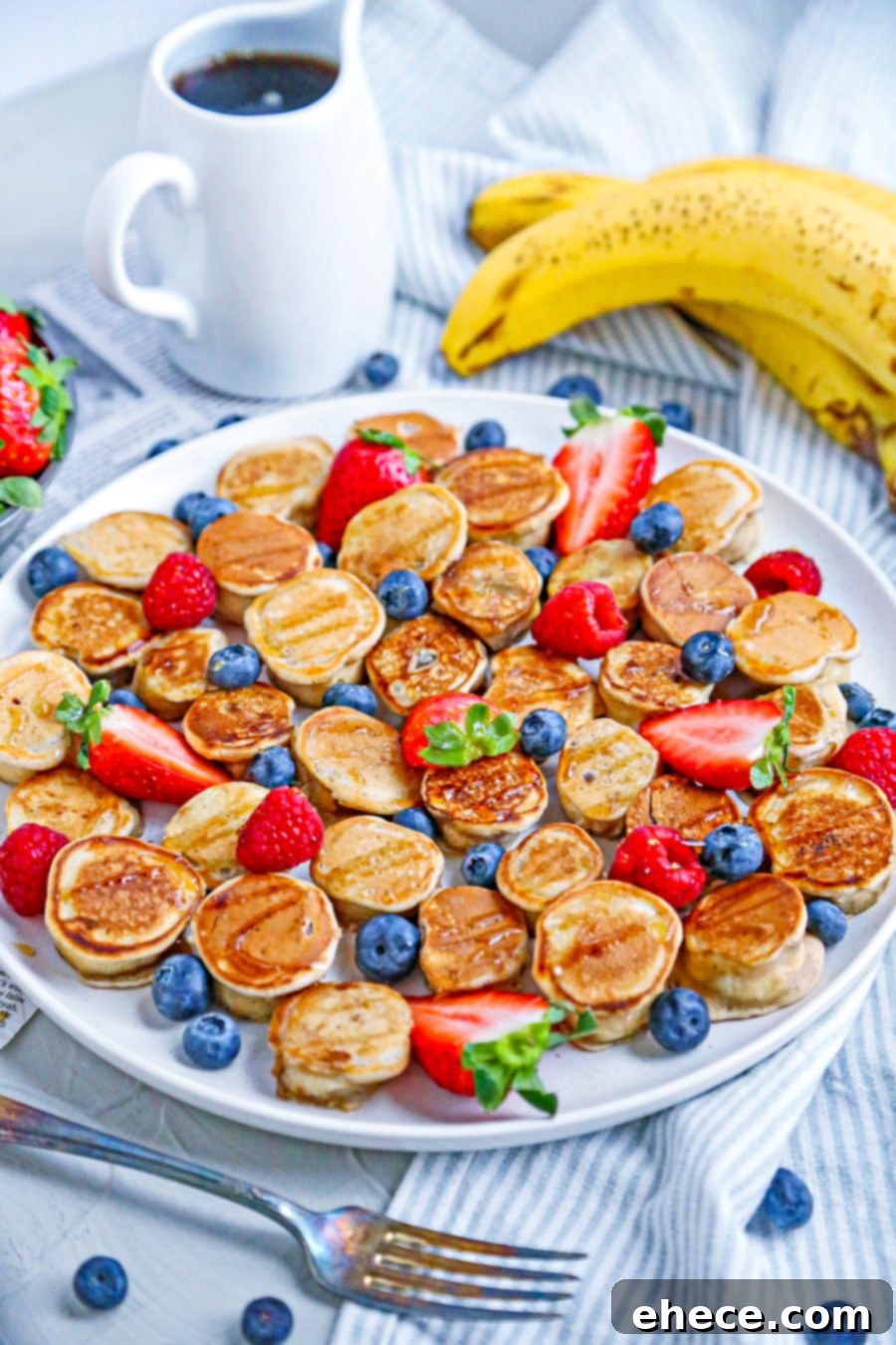 A close-up shot of several banana pancake bites topped with powdered sugar and fresh berries