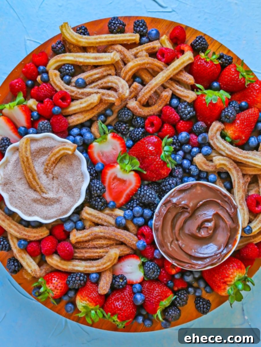 A vibrant Churro and Berry Dessert Board featuring crispy churros, fresh strawberries, blueberries, and a rich chocolate dipping sauce.