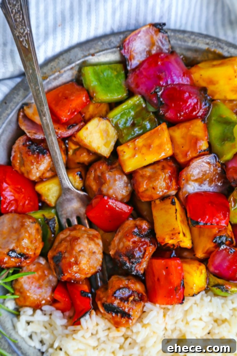 Three fully cooked BBQ Sausage, Veggie, and Pineapple Skewers on a white plate with a fork.