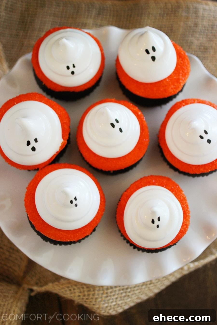 Close-up of fluffy meringue ghosts atop vibrant orange frosted dark chocolate cupcakes for Halloween