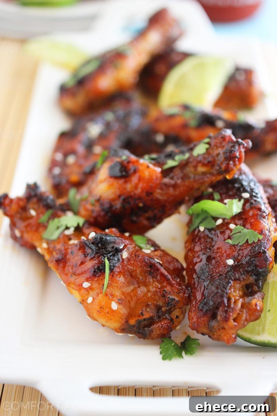A serving platter piled high with finished honey-sriracha wings, garnished with chopped cilantro, sesame seeds, and fresh lime wedges.