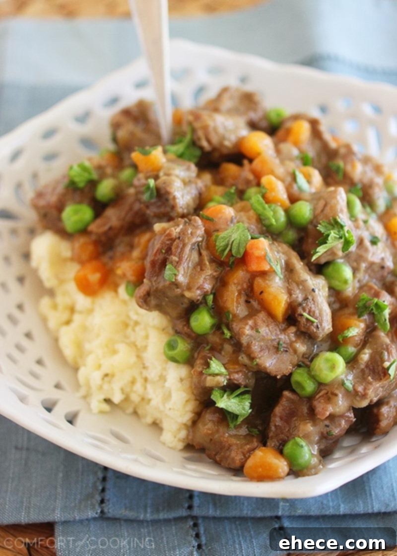 Close-up shot of Irish Beef Stew, showcasing tender chunks of beef, carrots, and peas in a thick, dark gravy. The stew is served in a white bowl, ready to be enjoyed as a hearty meal.