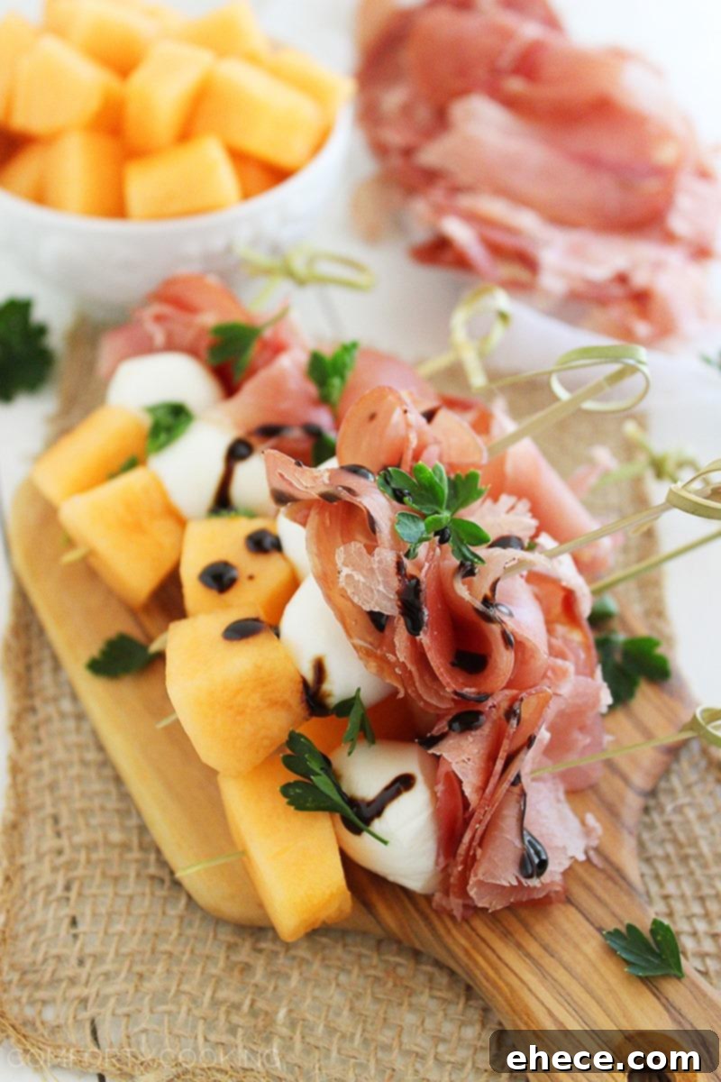 A serving platter filled with Melon, Prosciutto, and Mozzarella Skewers, garnished with fresh herbs and a drizzle of balsamic glaze, ready for a gathering. | thecomfortofcooking.com