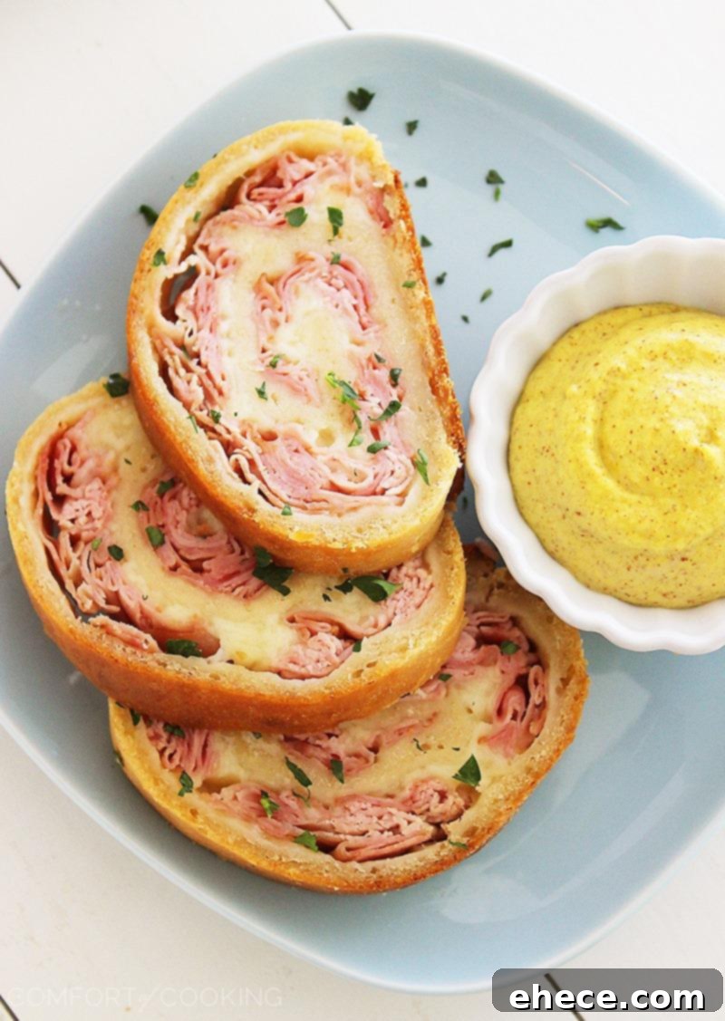 Three-Ingredient Baked Ham and Cheese Swirls 5 Baked Ham and Cheese Rollups, sliced to reveal the melted cheese and ham layers, served with a side of dipping sauce.