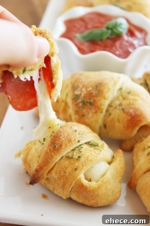 Pepperoni Pizza Crescent Bites 5 Two rows of freshly baked Pepperoni Pizza Crescent Rollups, perfectly golden and inviting, stacked on a plate with marinara sauce for dipping.