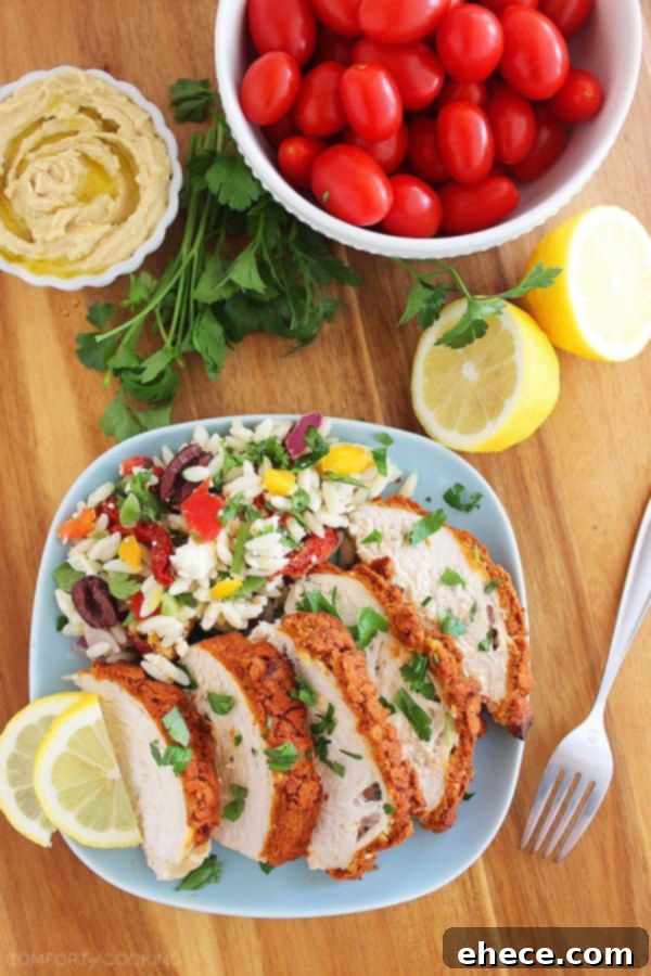 Close-up of baked chicken breast with a golden, crispy hummus crust, garnished with fresh herbs and a lemon wedge.