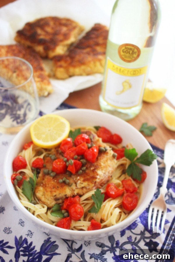 A close-up of a single serving of crispy chicken scallopini with pasta, sauce, tomatoes, and capers.