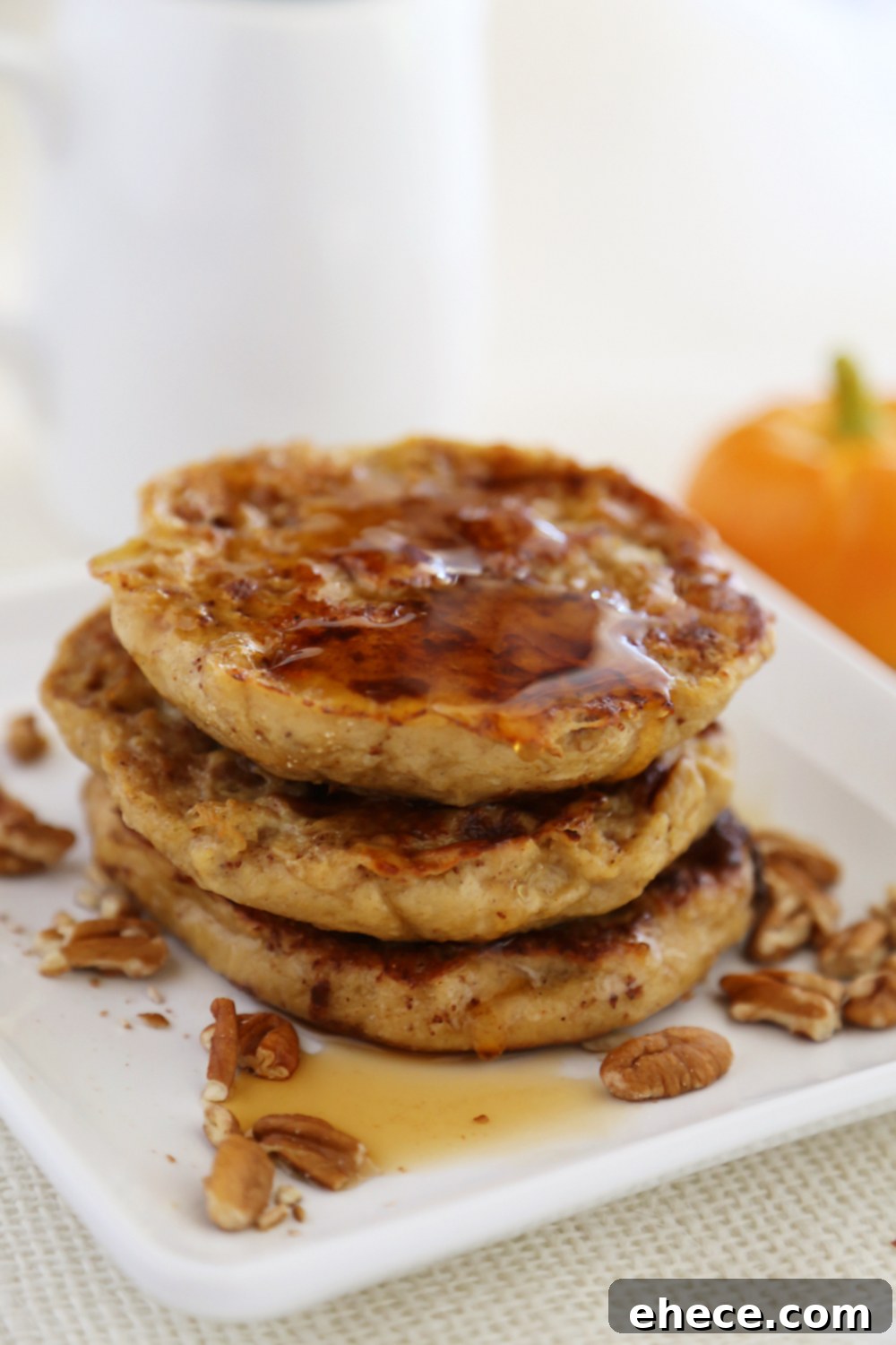 A stack of Pumpkin Vanilla English Muffin French Toast with various toppings like whipped cream, pecans, and maple syrup.
