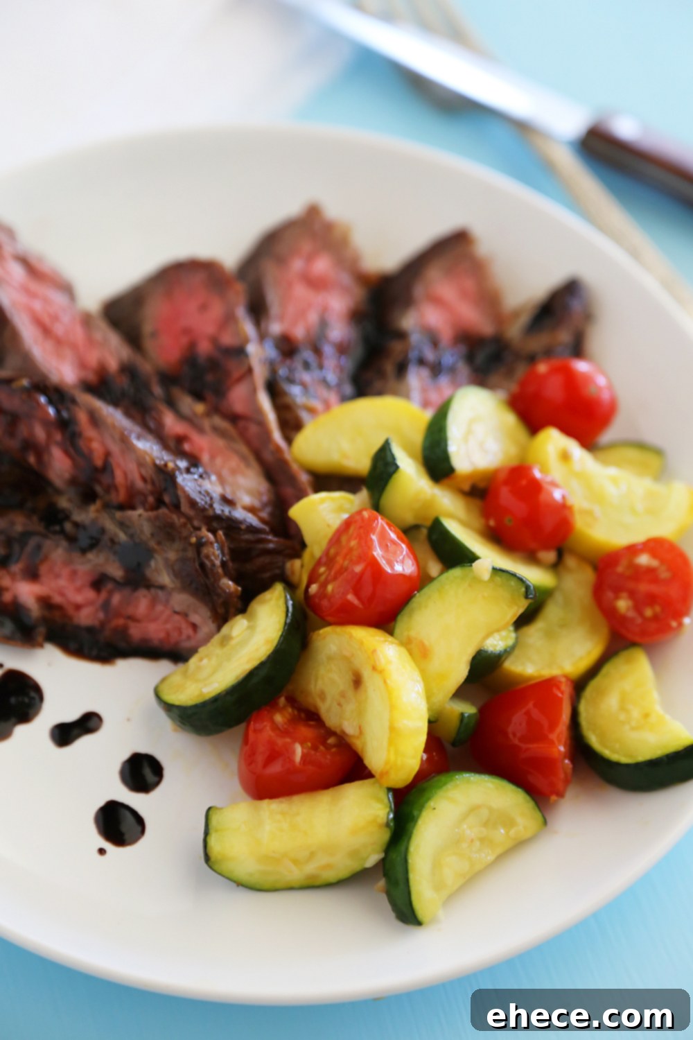 Freshly cooked Skillet Balsamic Skirt Steak, thinly sliced, with vibrant garlic-sautéed vegetables arranged artfully on a plate, ready to be served.