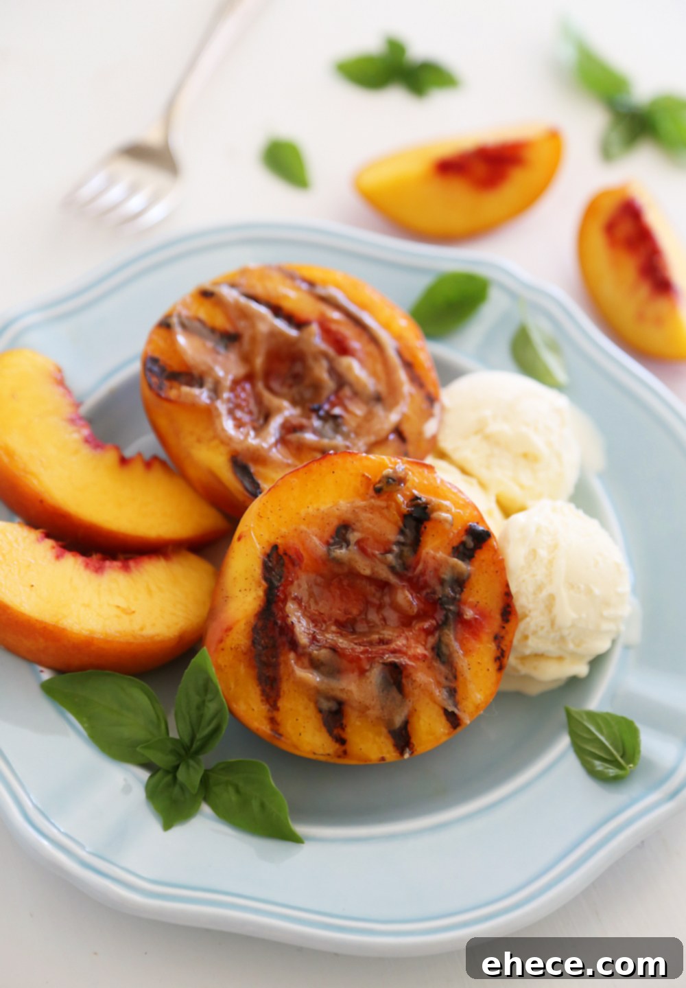 Perfectly grilled peach halves topped with melting cinnamon-sugar butter, served with a scoop of vanilla ice cream and fresh mint leaves on a white plate.